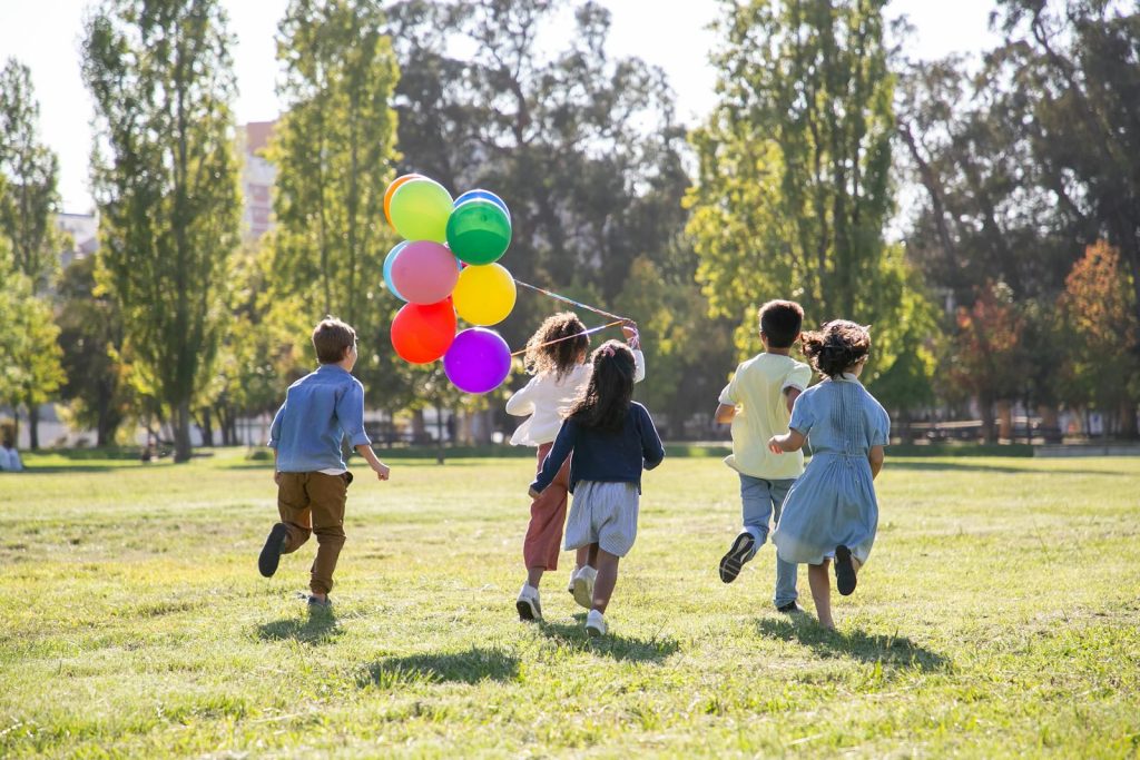 Children happily running with balloons in a sunny park, capturing friendship and joy.